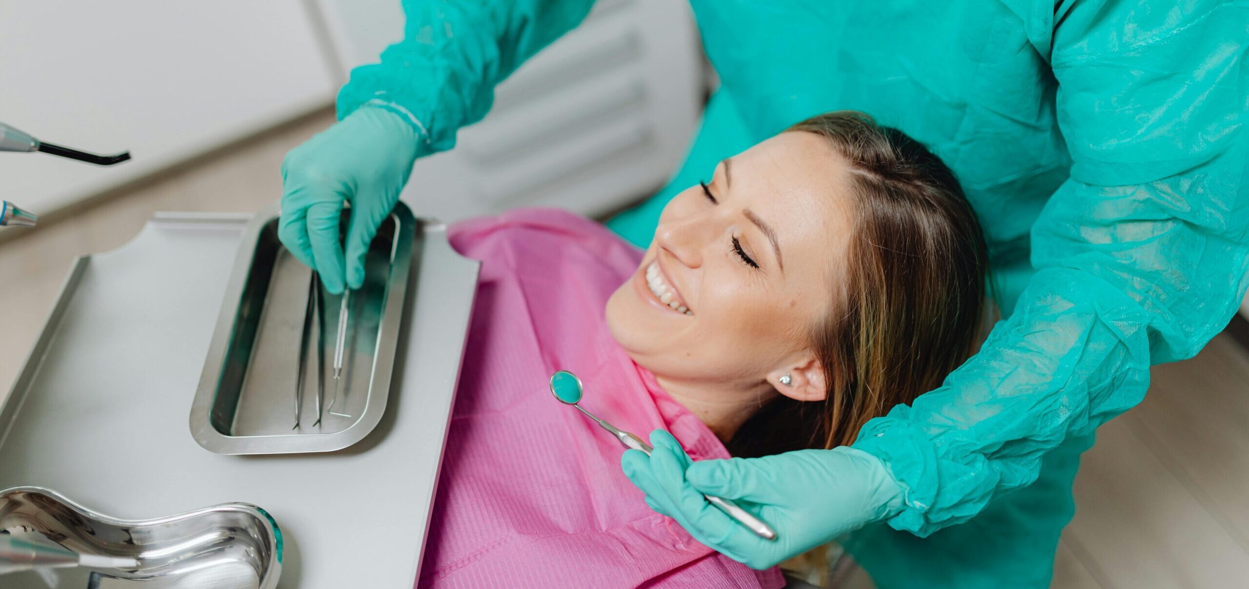 Paciente deitada na cadeira odontológica enquanto profissional prepara atendimento com instrumentos.