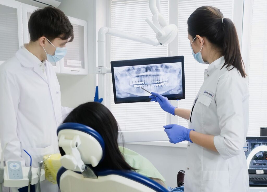 Dentista analisando radiografia com paciente em consultório odontológico.