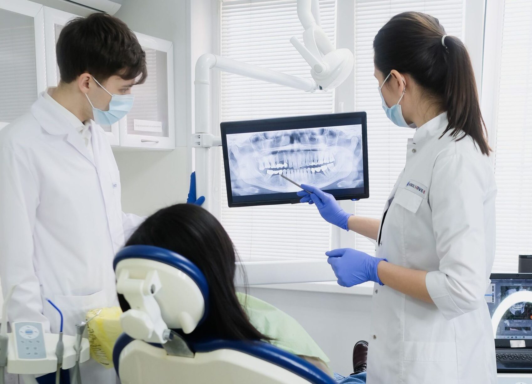 Dentista analisando radiografia com paciente em consultório odontológico.
